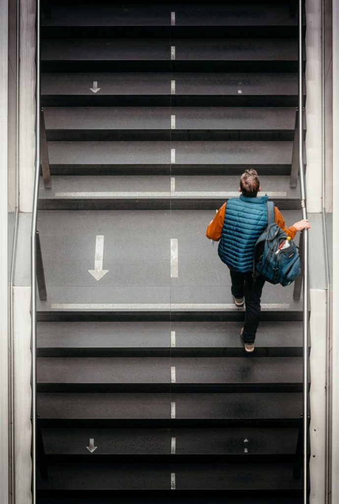 A person in a blue vest ascends wide stairs with directional arrows.